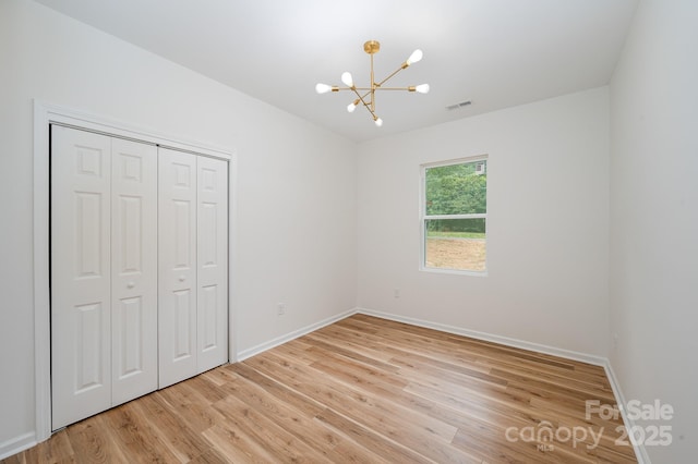 unfurnished bedroom featuring light wood finished floors, a closet, baseboards, and a notable chandelier