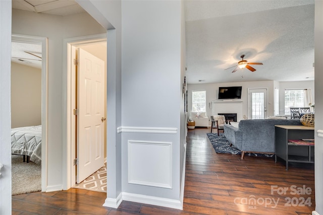 living room featuring dark wood-type flooring, ceiling fan, a fireplace, and a textured ceiling