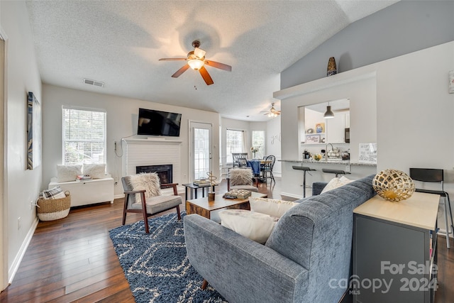 living room with ceiling fan, a wealth of natural light, dark hardwood / wood-style flooring, and a brick fireplace