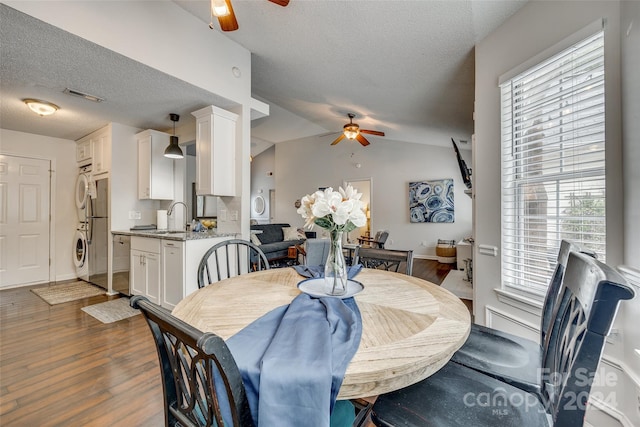 dining room with ceiling fan, vaulted ceiling, dark hardwood / wood-style flooring, and stacked washer / drying machine