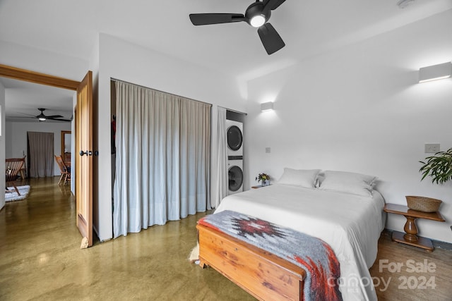 bedroom featuring ceiling fan, stacked washer and dryer, and concrete floors