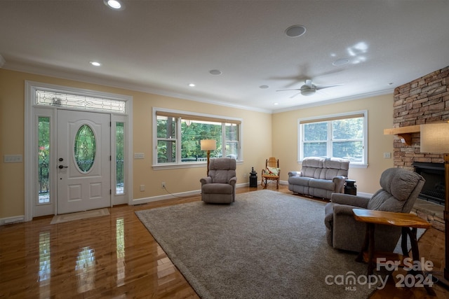 living room featuring crown molding, a healthy amount of sunlight, ceiling fan, and a stone fireplace