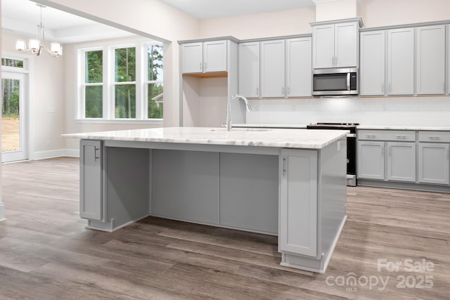 kitchen with gray cabinets, appliances with stainless steel finishes, a center island with sink, and decorative backsplash