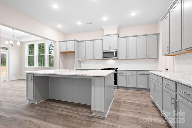 kitchen with appliances with stainless steel finishes, gray cabinets, an island with sink, and hardwood / wood-style floors