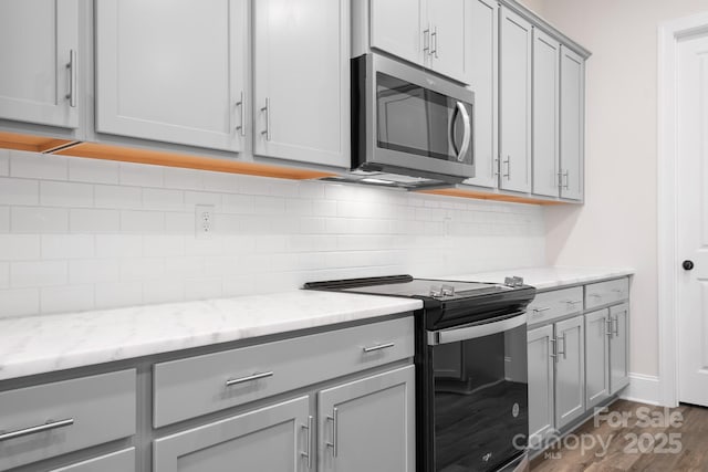 kitchen featuring dark wood-type flooring, gray cabinetry, light stone counters, black electric range, and decorative backsplash