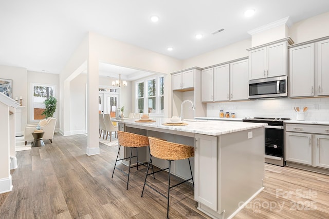 kitchen with stainless steel appliances, a kitchen breakfast bar, light stone counters, a center island with sink, and decorative backsplash