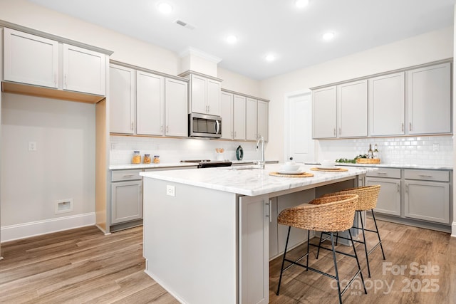 kitchen featuring sink, gray cabinets, light hardwood / wood-style floors, and an island with sink