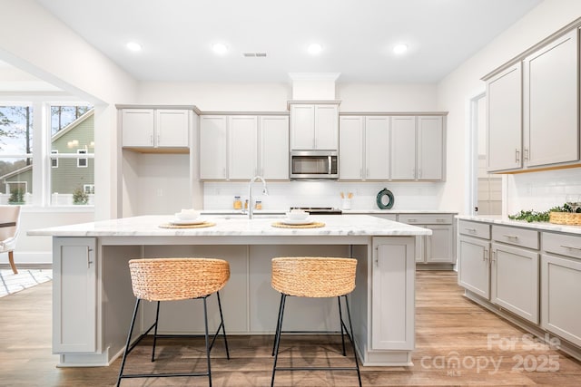 kitchen with light stone counters, sink, and a center island with sink