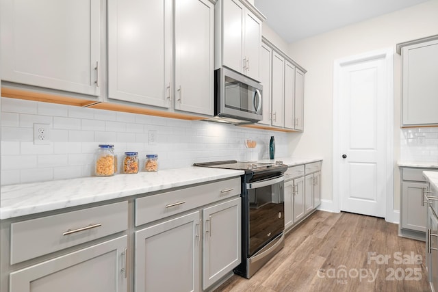 kitchen featuring light stone counters, stainless steel appliances, light hardwood / wood-style floors, and gray cabinetry