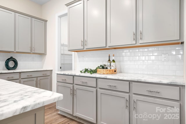 kitchen with gray cabinetry, backsplash, light stone counters, and light hardwood / wood-style floors