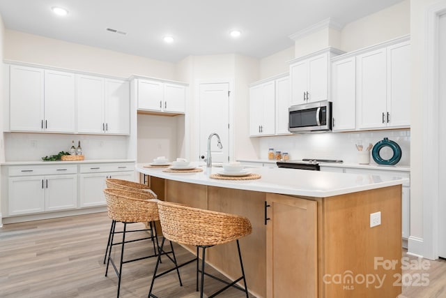 kitchen featuring white cabinetry, a kitchen island with sink, tasteful backsplash, and light wood-type flooring