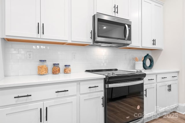 kitchen featuring black electric range oven, light wood-type flooring, white cabinetry, and backsplash