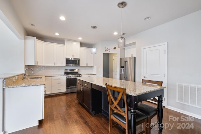 kitchen featuring light stone countertops, appliances with stainless steel finishes, a kitchen breakfast bar, decorative light fixtures, and dark hardwood / wood-style floors