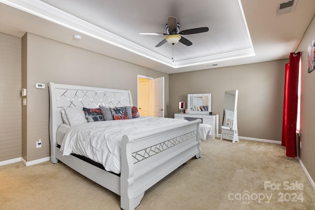 bedroom featuring light colored carpet, a tray ceiling, and ceiling fan