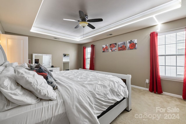 carpeted bedroom with multiple windows, a raised ceiling, and ceiling fan