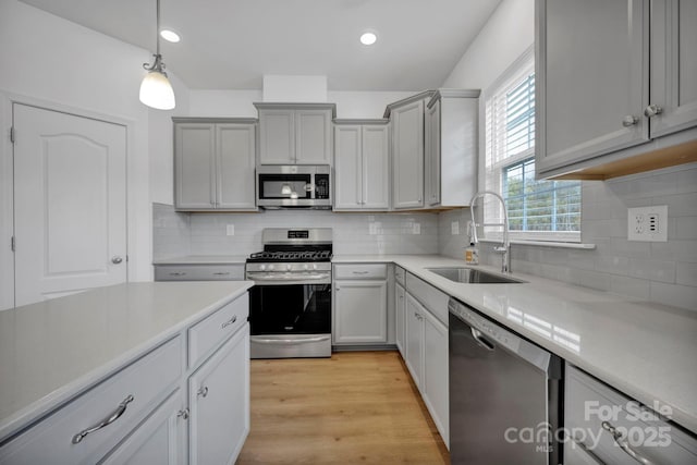 kitchen with appliances with stainless steel finishes, backsplash, gray cabinetry, sink, and hanging light fixtures