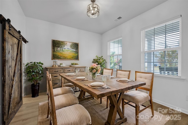 dining room featuring a barn door, a notable chandelier, and light wood-type flooring