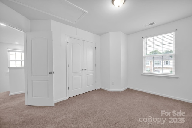 unfurnished bedroom featuring multiple windows, light carpet, and a closet