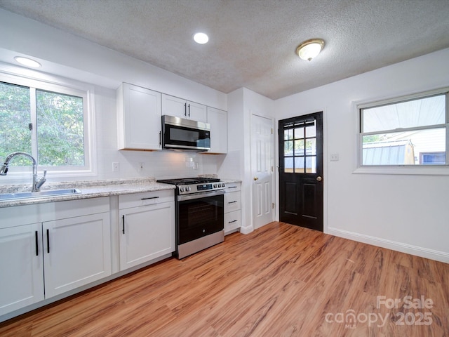 kitchen with sink, a textured ceiling, decorative backsplash, white cabinets, and appliances with stainless steel finishes