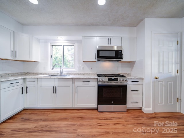 kitchen with sink, light wood-type flooring, a textured ceiling, white cabinetry, and stainless steel appliances