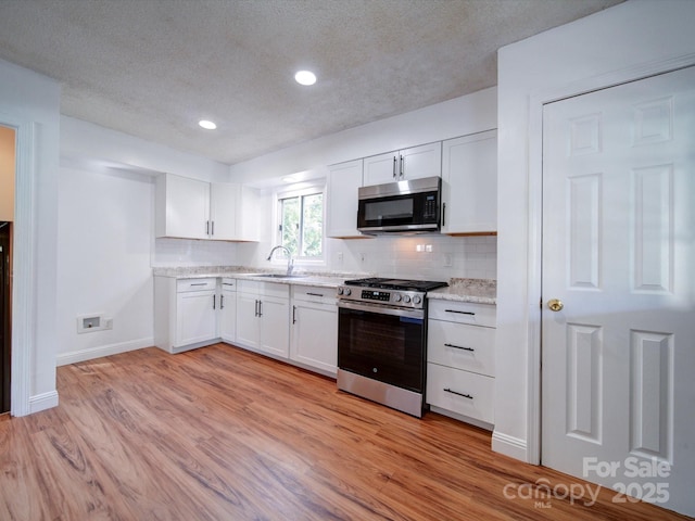 kitchen featuring backsplash, white cabinets, sink, light hardwood / wood-style floors, and stainless steel appliances