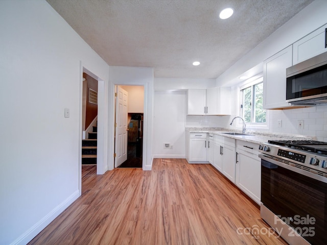 kitchen featuring appliances with stainless steel finishes, light hardwood / wood-style flooring, white cabinetry, and sink