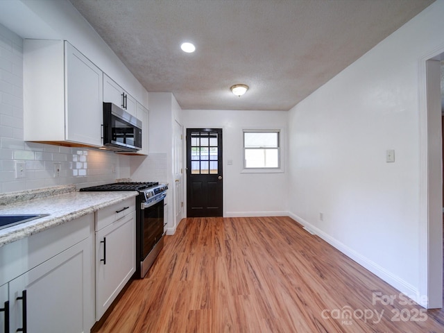 kitchen featuring light stone countertops, appliances with stainless steel finishes, light wood-type flooring, backsplash, and white cabinetry