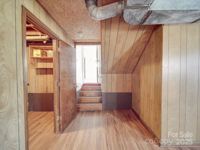 bonus room with light wood-type flooring and wooden walls