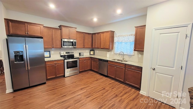 kitchen with sink, backsplash, stainless steel appliances, light stone countertops, and light hardwood / wood-style floors