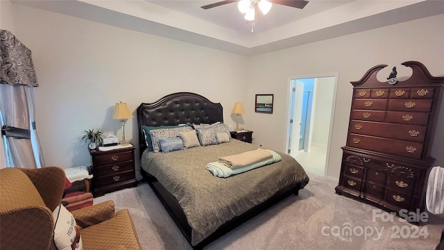 bedroom with a tray ceiling, ensuite bath, ceiling fan, and light colored carpet