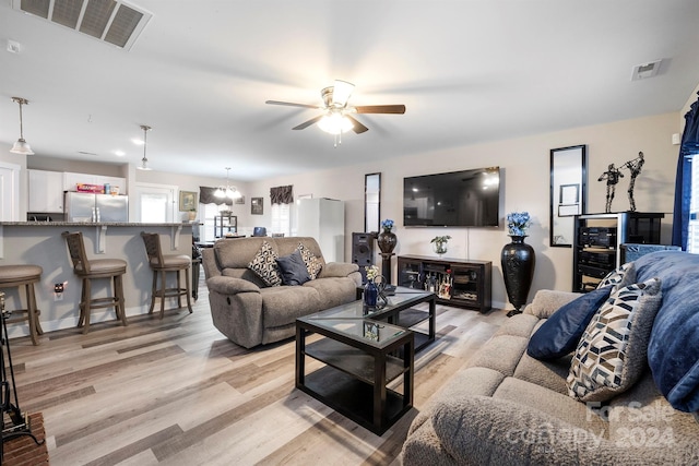 living room featuring ceiling fan with notable chandelier and light wood-type flooring