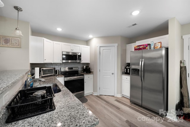 kitchen with white cabinets, hanging light fixtures, light hardwood / wood-style flooring, appliances with stainless steel finishes, and light stone counters