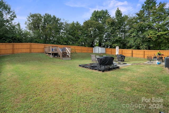 view of yard with a wooden deck, a fire pit, and a storage shed