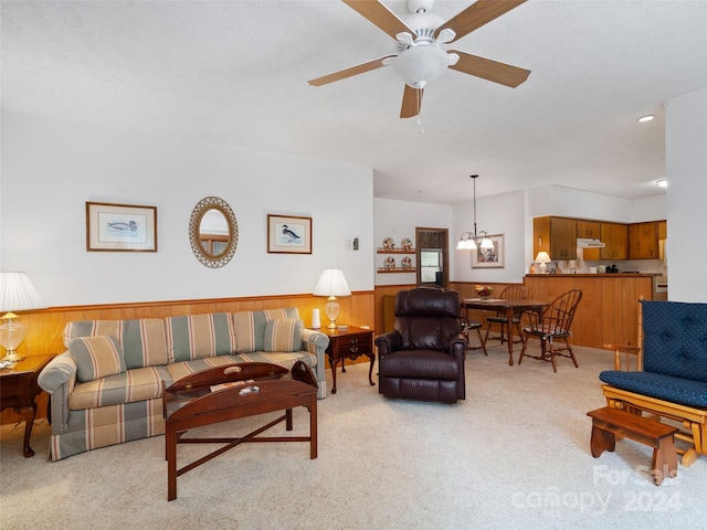 living room featuring light colored carpet, ceiling fan with notable chandelier, and wooden walls