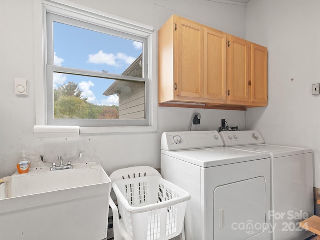 washroom with a wealth of natural light, cabinets, washer and clothes dryer, and sink