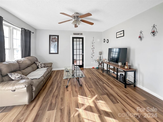 living area featuring ceiling fan, baseboards, wood finished floors, and a textured ceiling