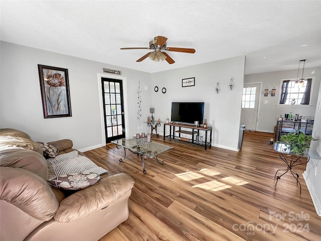 living area featuring a textured ceiling, light wood finished floors, baseboards, and a ceiling fan