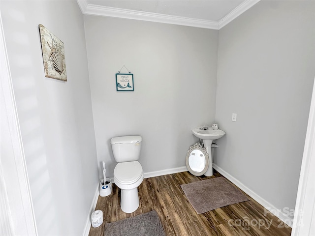 half bath with wood finished floors, crown molding, baseboards, and toilet