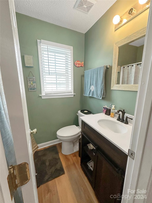 bathroom featuring wood finished floors, a textured ceiling, vanity, toilet, and visible vents