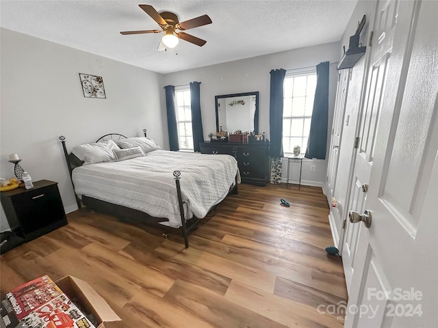 bedroom featuring multiple windows, a textured ceiling, ceiling fan, and hardwood / wood-style flooring