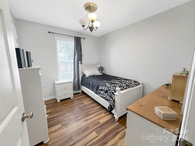 bedroom featuring wood finished floors, a textured ceiling, and an inviting chandelier
