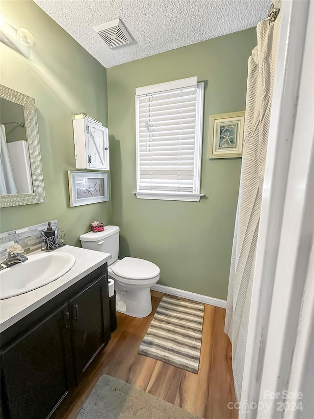 bathroom with wood finished floors, visible vents, toilet, vanity, and baseboards