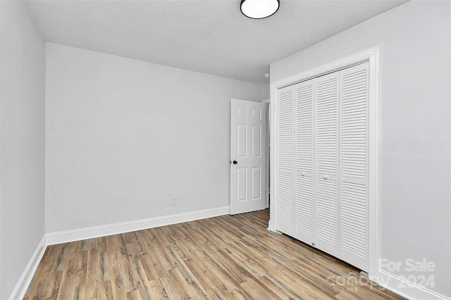 unfurnished bedroom featuring a textured ceiling, a closet, and light hardwood / wood-style floors