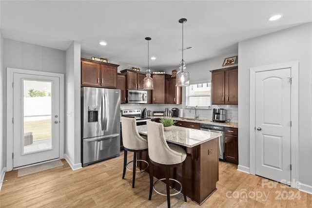 kitchen featuring pendant lighting, sink, a kitchen island, appliances with stainless steel finishes, and light hardwood / wood-style floors