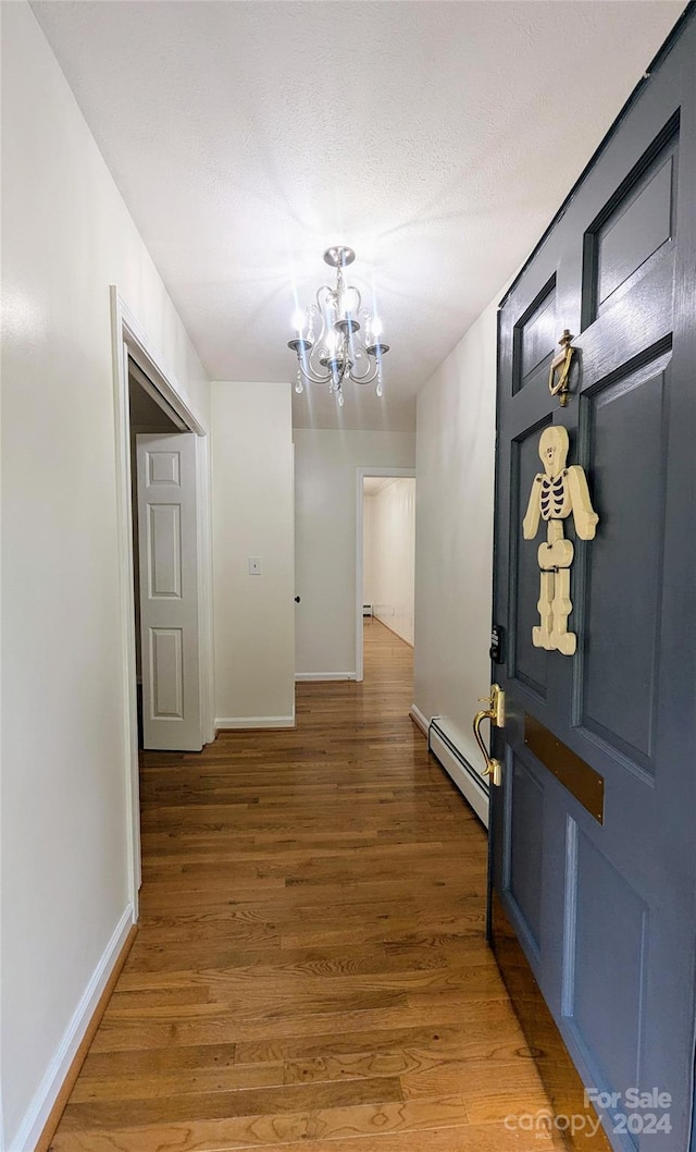 hallway featuring a notable chandelier, a textured ceiling, wood-type flooring, and a baseboard radiator