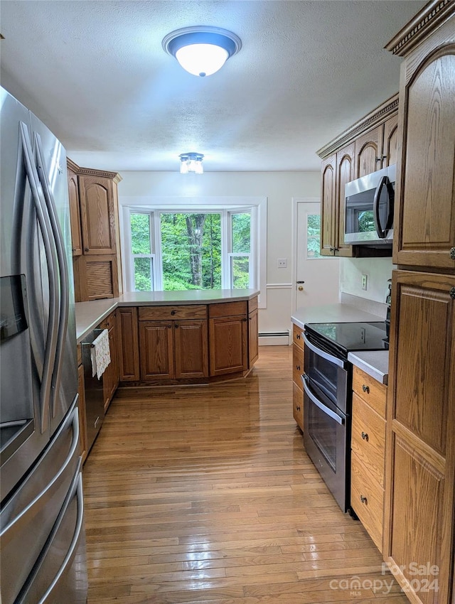 kitchen with appliances with stainless steel finishes, a textured ceiling, baseboard heating, and light wood-type flooring