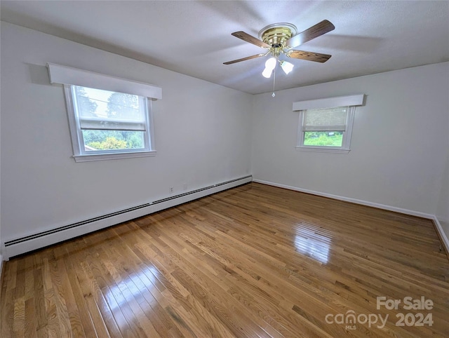 spare room with hardwood / wood-style flooring, a healthy amount of sunlight, a baseboard heating unit, and ceiling fan