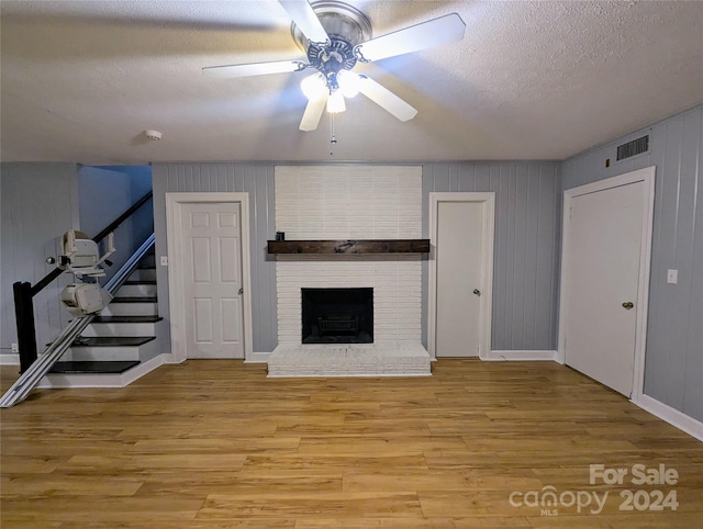 unfurnished living room with ceiling fan, a textured ceiling, a brick fireplace, light hardwood / wood-style flooring, and wood walls