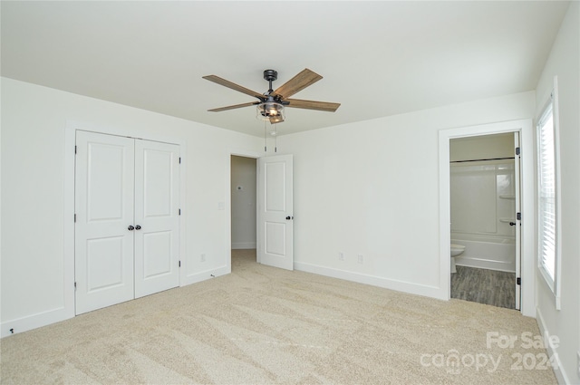 unfurnished bedroom featuring multiple windows, ensuite bathroom, light colored carpet, and ceiling fan