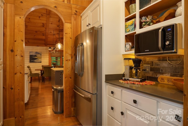 kitchen with appliances with stainless steel finishes, hanging light fixtures, white cabinetry, light wood-type flooring, and an inviting chandelier